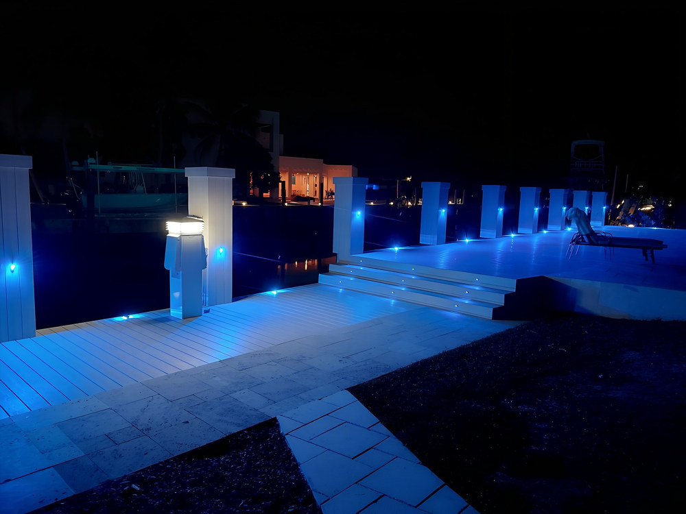 South Florida waterfront deck at night with vivid blue LED piling cap lights and illuminated step risers