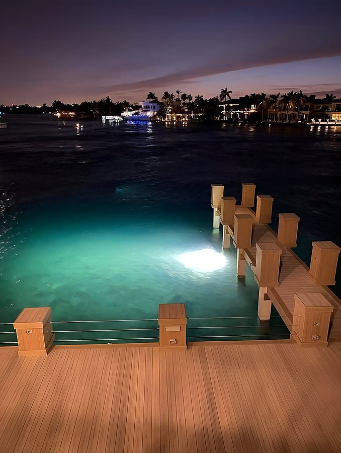Luxury custom dock at night with teal underwater lighting and teak wood decking — South Florida by Contour Marine