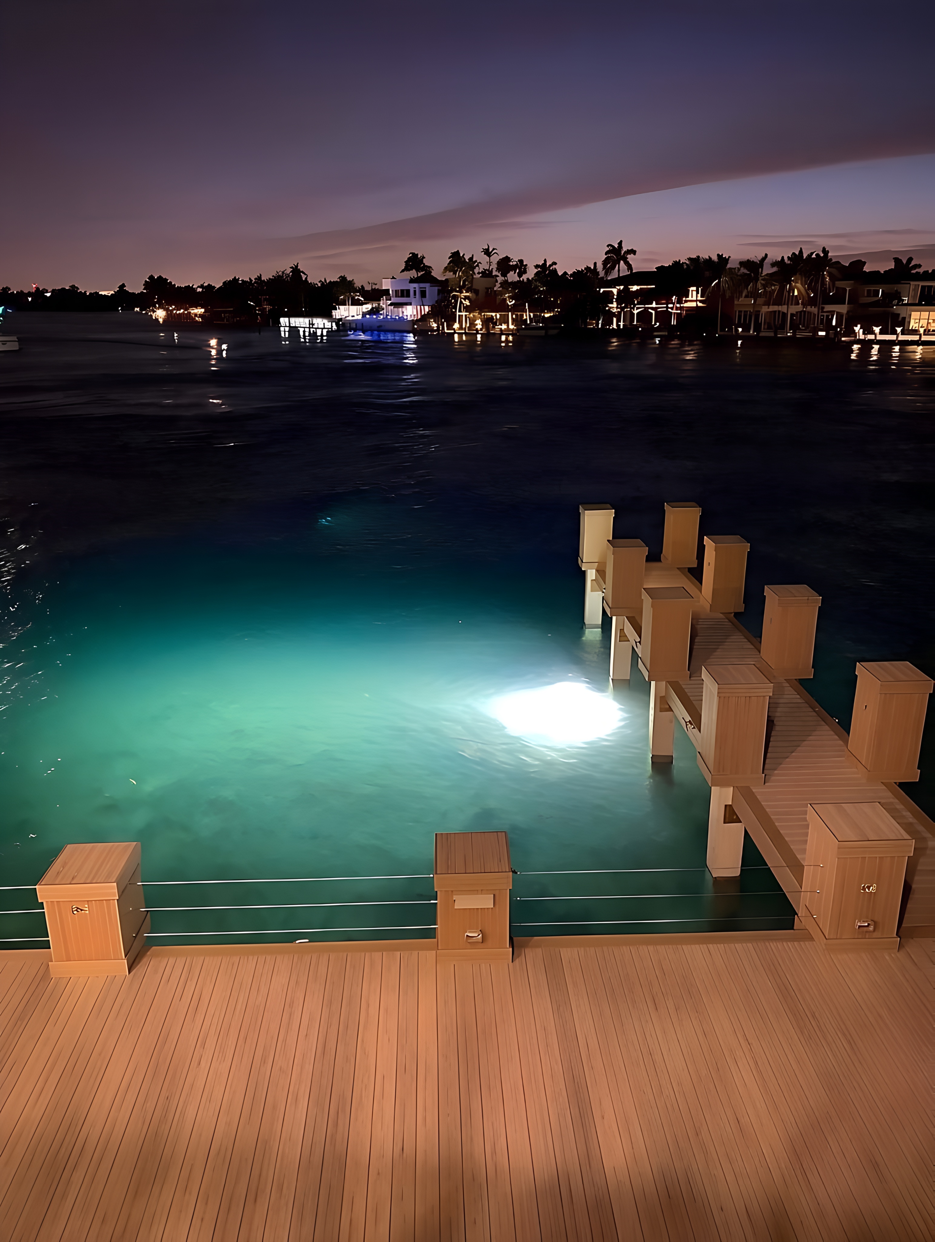 Luxury custom dock at night with teal underwater lighting and teak wood decking — South Florida by Contour Marine