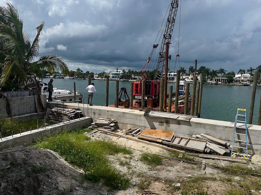 Engineered seawall installation — crane barge driving pilings on a South Florida canal, Contour Marine crew on site