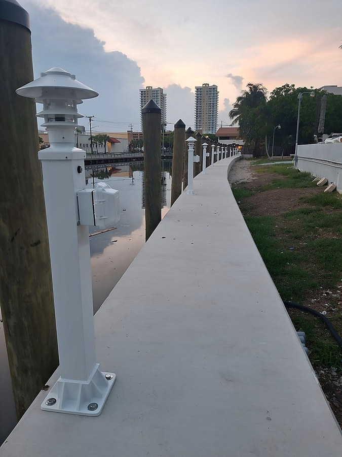 Finished seawall cap with white dock light posts and timber pilings — South Florida by Contour Marine